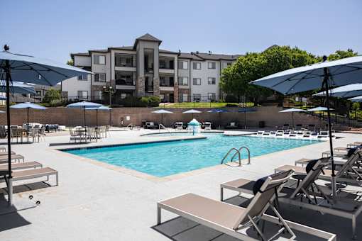 A pool with sun loungers and umbrellas in front of a building.