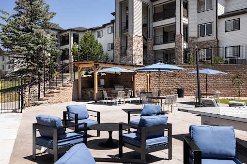 A patio with blue chairs and a fire pit in front of a building.