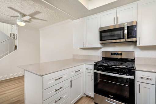 A kitchen with white cabinets and a microwave and a black gas stove top oven.