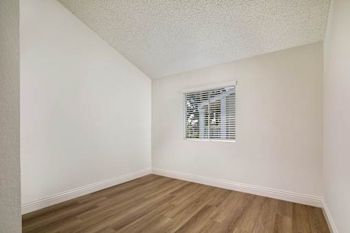 A bedroom with a window and hardwood flooring.