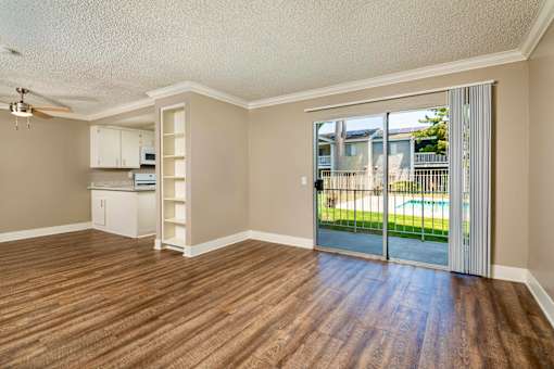A living space with hardwood floors and a sliding glass door with a pool view..