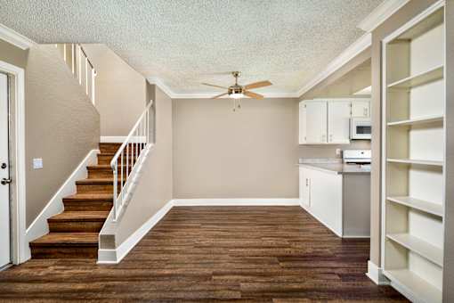 A dining room with a ceiling fan and staircase and a kitchen area.
