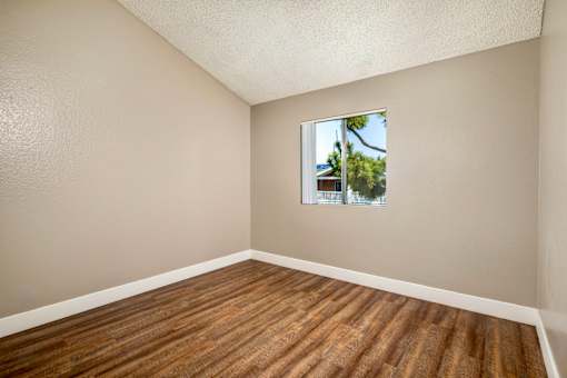 A bedroom with hardwood flooring and a window showing a tree outside.