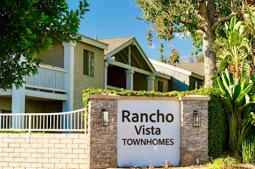 A sign for Rancho Vista Townhomes in front of apartment homes with balconies and lush green landscaping.