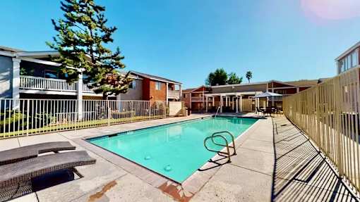 A swimming pool surrounded by a fence and lunge chairs and umbrella.