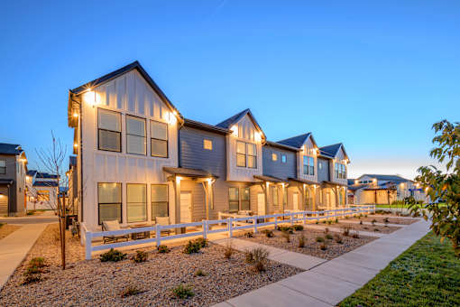 A row of houses with lit up windows and a white fence in front.