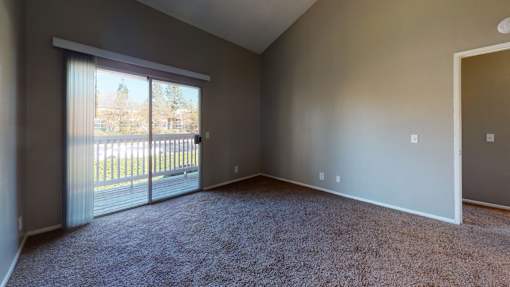 A room with a carpeted floor and a sliding glass door leading to a balcony.