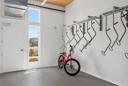 A red bicycle is parked in a garage with a white wall and a bike rack.