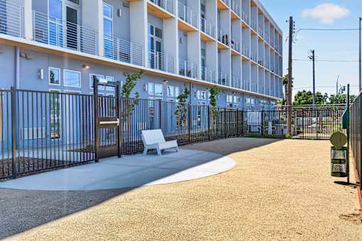 A modern apartment complex with a fenced courtyard and a bench.
