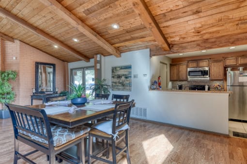 a dining area with a wooden table and chairs and a kitchen in the background