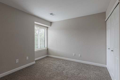 A room with a carpeted floor and a window with blinds.