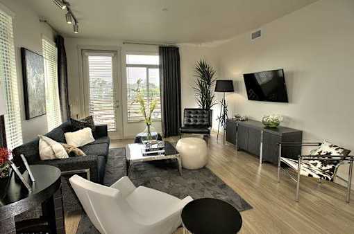 A modern living room with a black couch, a white chair, and a TV mounted on the wall.