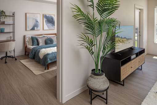 A bedroom with a bed, a plant, and a painting on the wall.