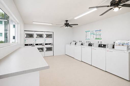 A clean, white commercial kitchen with stainless steel appliances and a fan on the ceiling.