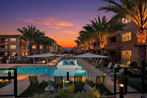 A pool surrounded by palm trees and lounge chairs at dusk.