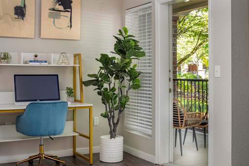 A room with a desk, chair, and a potted plant.