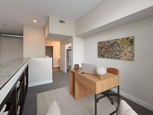 A room with a desk and a chair with a painting on the wall.