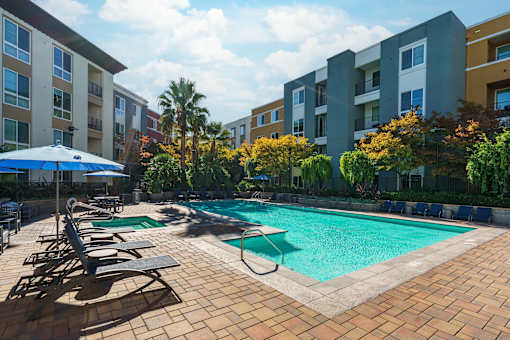 A swimming pool surrounded by lounge chairs and umbrellas in a residential area.