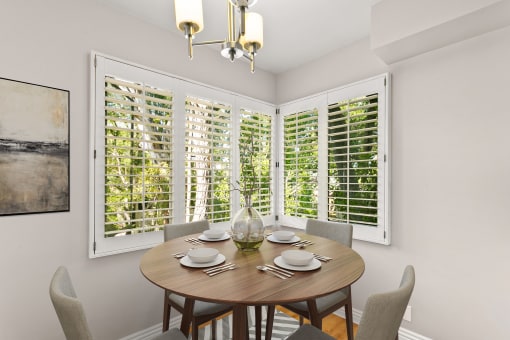 a dining area with a wooden table and chairs and multiple windows with white shutters at Orange Grove Circle, Pasadena, CA