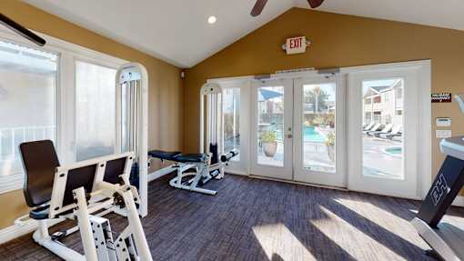 A gym with a weight bench, a chair and a window.