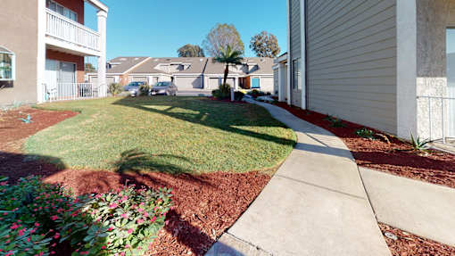 A residential area with a sidewalk and a grassy area with flowers.