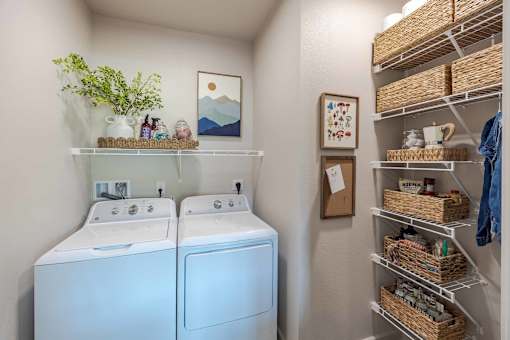 A small laundry room with a washer and dryer and a shelf with baskets on it.