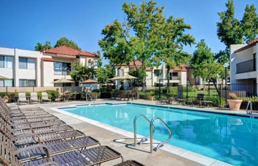 A swimming pool surrounded by sun loungers and trees at The Casas Apartments, California, 92126