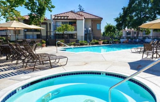A swimming pool surrounded by lounge chairs and umbrellas at The Casas Apartments, California