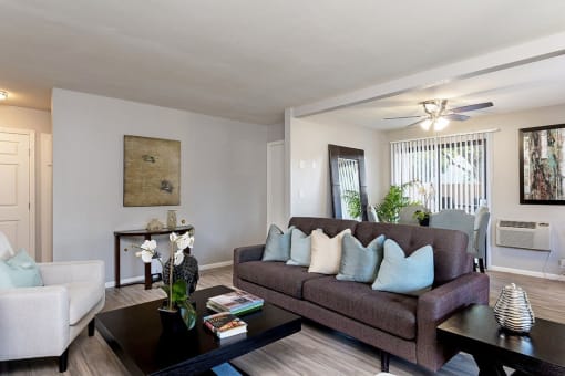 A living room with a brown couch, a coffee table, and a painting on the wall at The Casas Apartments, San Diego, California