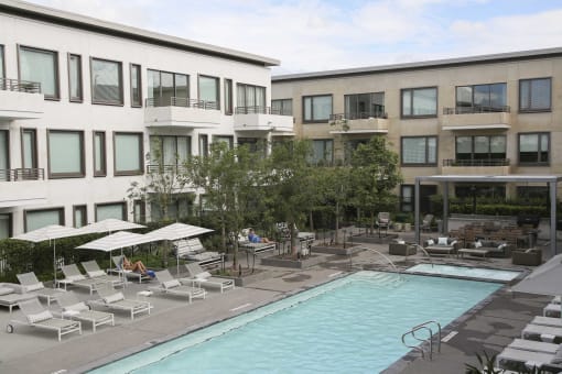 a hotel pool with chairs and umbrellas in front of a building