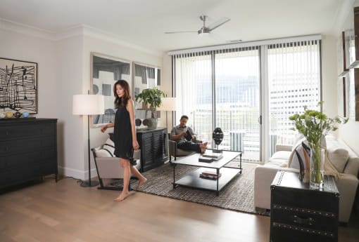 a woman standing in a living room with a man sitting on a couch