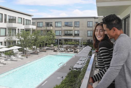 a man and woman standing on a balcony overlooking a hotel pool