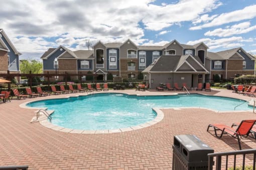 a large swimming pool with red chairs in front of an apartment building