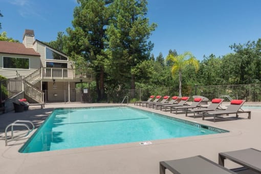 a swimming pool with red chairs around it in front of a house