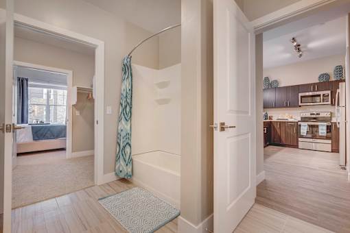 an open door leading to a bathroom with a shower and a kitchen