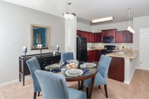 a dining room table with blue chairs and a kitchen with black appliances