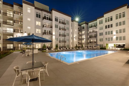 a swimming pool at night with an umbrella in front of an apartment building