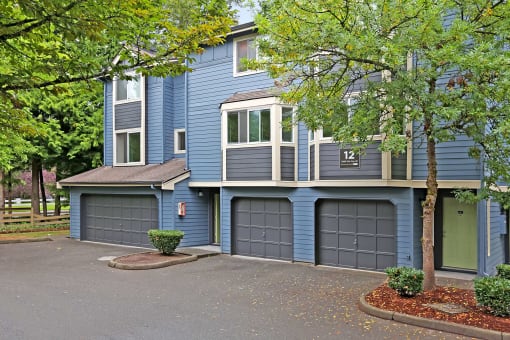 a blue house with two garage doors and trees