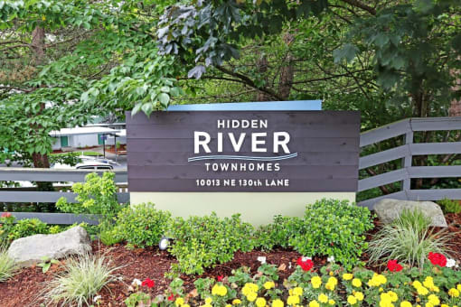 a sign for hidden river townhomes in front of plants and flowers