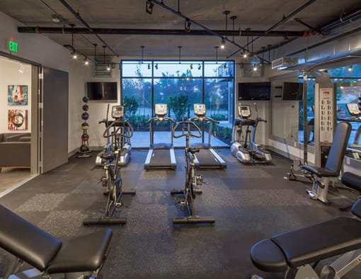 a gym with cardio equipment and a large window