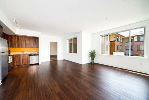 an empty living room with wood floors and a kitchen