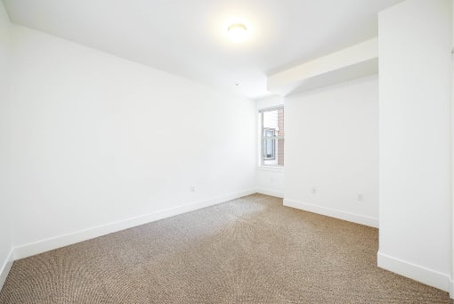 a living room with white walls and carpet and a window