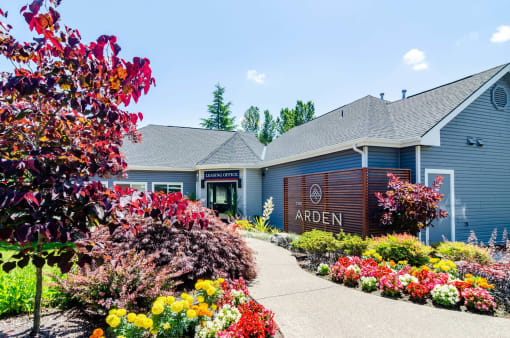 the front of an apartment building with a sidewalk and colorful flowers