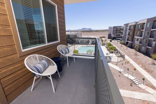 a balcony with two chairs and a table and a pool  in the background at Element 12 Apartments, Henderson NV