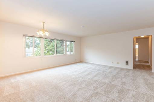 A large, empty room with a carpeted floor and a chandelier hanging from the ceiling at Hillsdale Garden Apartments, San Mateo, CA 94403