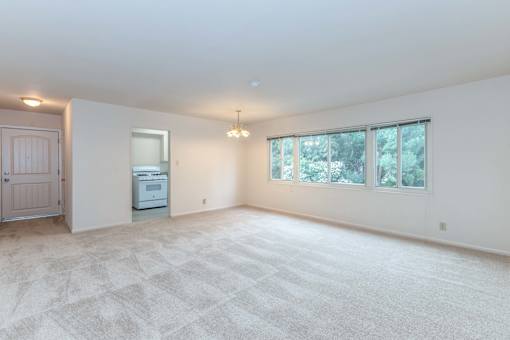 A spacious room with a carpeted floor and a window overlooking trees at Hillsdale Garden Apartments, California