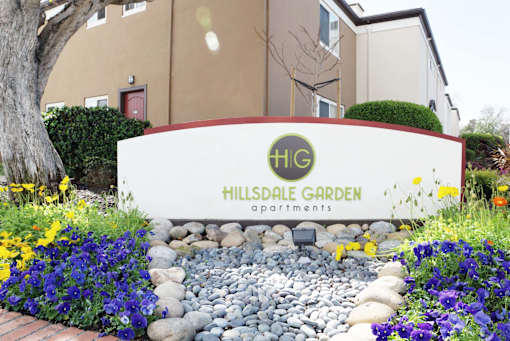 A sign for a garden apartment complex with a red door in the background at Hillsdale Garden Apartments, San Mateo