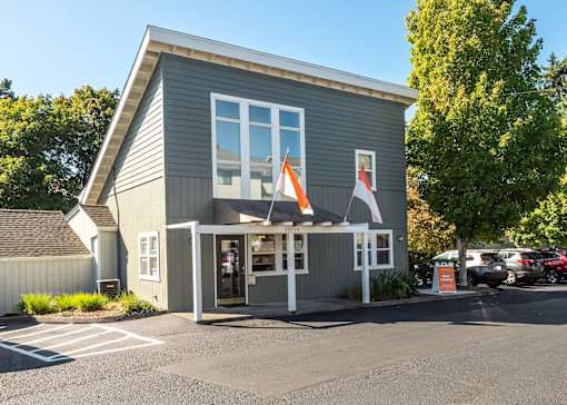 A grey building with a white awning and a red and white flag hanging from it at Aspenridge Apartments, Vancouver, WA 98683