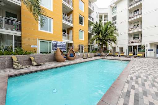 A swimming pool in front of a yellow building with a tiled floor.
