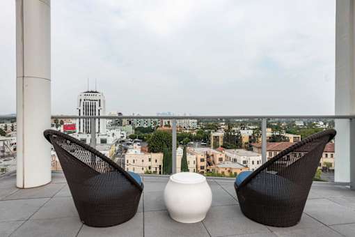 Two black chairs and a white vase on a balcony with a city view.
